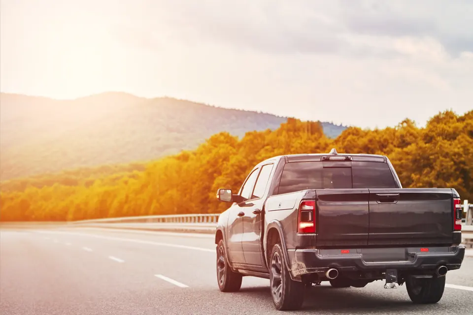 A dark pickup truck on a highway past autumn trees