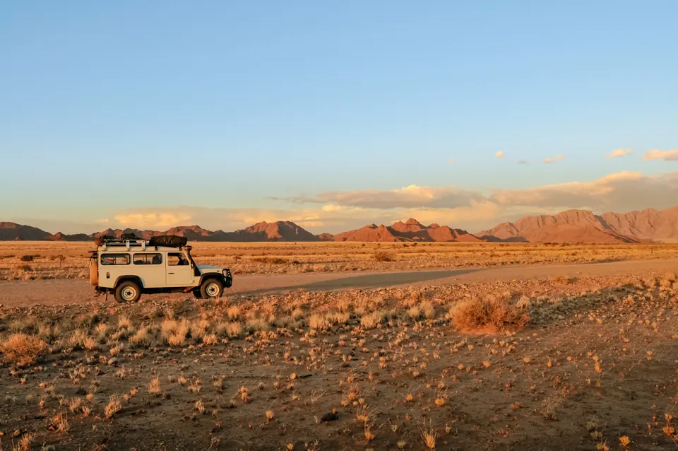 A 4x4 parked on a desert road at sunset