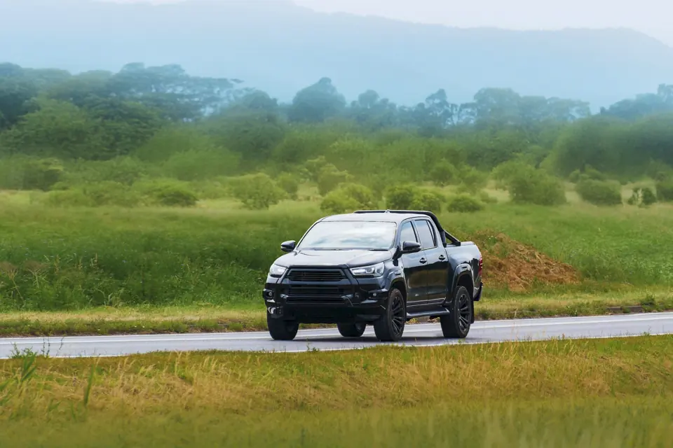 A black pickup truck on a rural road through green fields