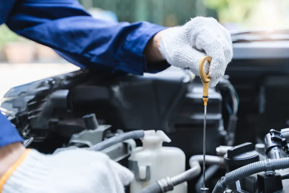 A gloved hand pulling a dipstick under the hood
