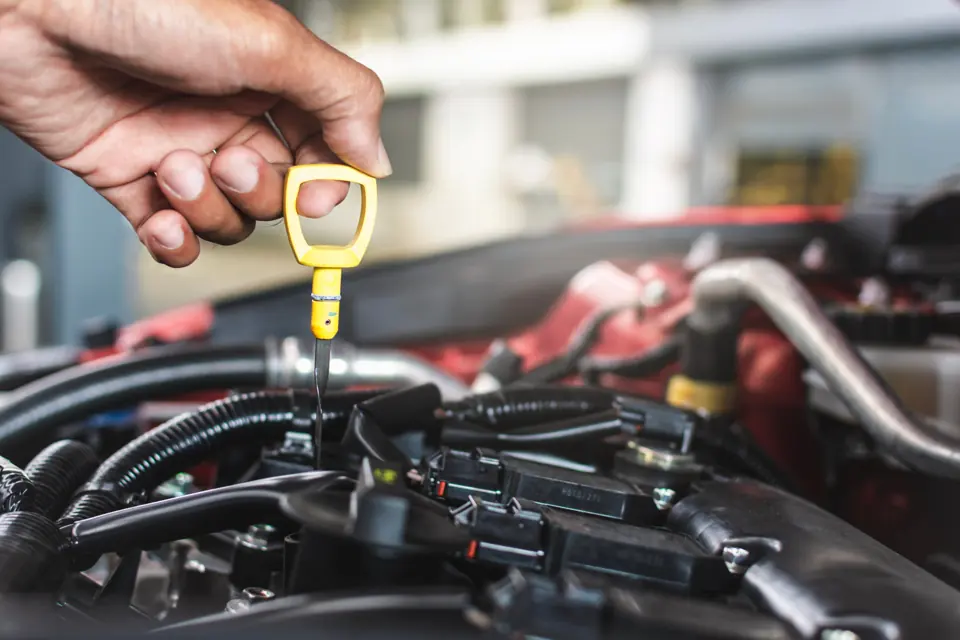 A hand lifting a yellow dipstick out of an engine bay