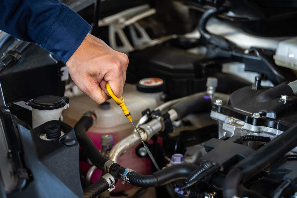 A technician checking the fluid level on a dipstick under the hood