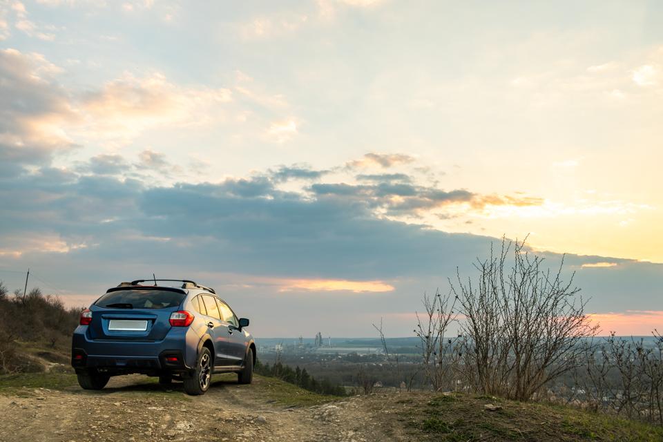 A blue crossover SUV parked on a dirt overlook at sunset
