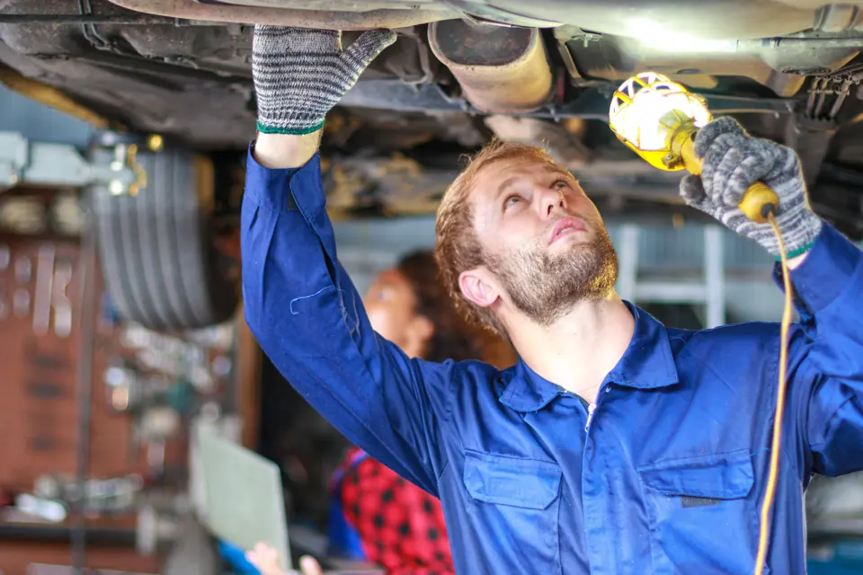 Male auto mechanic under a car at the repair shop