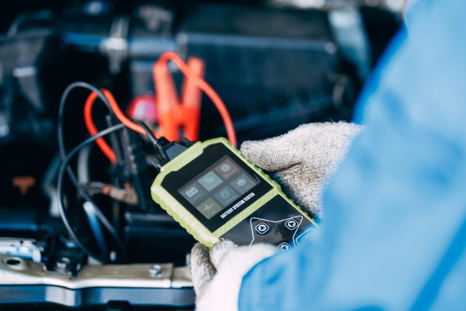 A technician holding a digital tester clipped to a battery