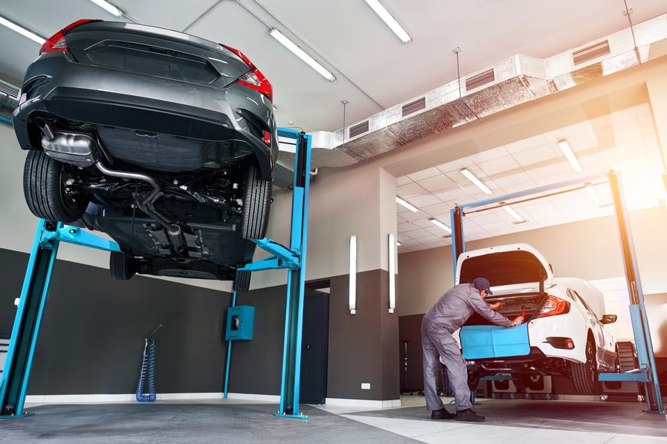 A car raised on a lift while a mechanic works at the front of another car